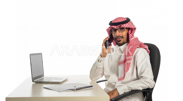 بورتريه لرجل أعمال خليجي سعودي في مقر العمل، إستخدام الحاسوب المحمول لإنجاز المهام، عقد إجتماع عمل عبر الإنترنت، العمل عن بعد، جلسة عمل، مفهوم إدارة الأعمال، إجراء مكالمة هاتفية، متابعة ومناقشة العمل، إستخدام أجهزة تقنية حديثة، التسويق الإلكتروني