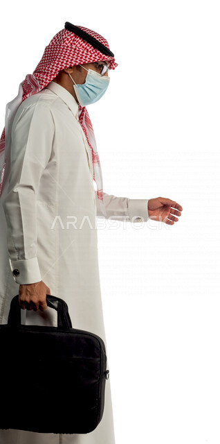 Portrait of a Saudi Gulf businessman carrying a bag to go to work with different facial and hand gestures, wearing a protective medical mask to prevent corona virus COVID-19, side view of a Saudi man in traditional Saudi dress, following virus prevention