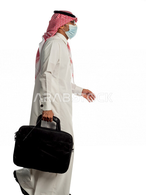 بورتريه لرجل أعمال خليجي سعودي يحمل حقيبة للذهاب إلى العمل بإيماءات وجه ويدين مختلفة، مرتدي القناع الطبي الوقائي للوقاية من فايروس كورونا كوفيد-19، منظر جانبي لرجل سعودي بالزي التقليدي السعودي، إتباع إجراءات الوقاية من الفايروسات، الحفاظ على المسافات
