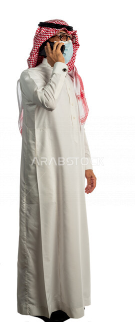 Portrait of a Saudi Gulf businessman talking on a mobile phone, wearing a medical mask to prevent corona virus covid-19, the concept of using modern technical devices, a working session, a business management concept, making a phone call, a white backgrou