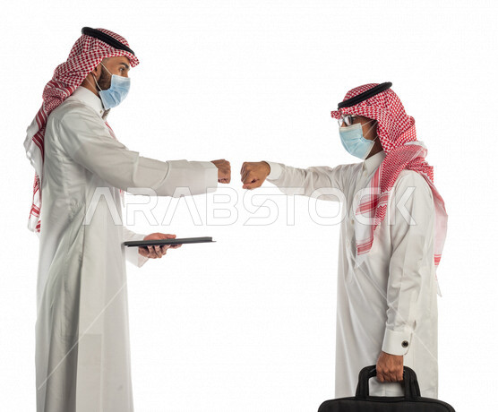بورتريه لموظفان خليجيان سعوديان يتصافحان بإيماءات يدين مختلفة، إرتداء القناع الطبي الوقائي للوقاية من فايروس كورونا كوفيد-19، إستخدام جهاز التابلت، زملاء عمل، مفهوم إدارة الأعمال، صفقات عمل، إتباع إجراءات الوقاية والحماية من الفيروسات، الحفاظ على المسافات