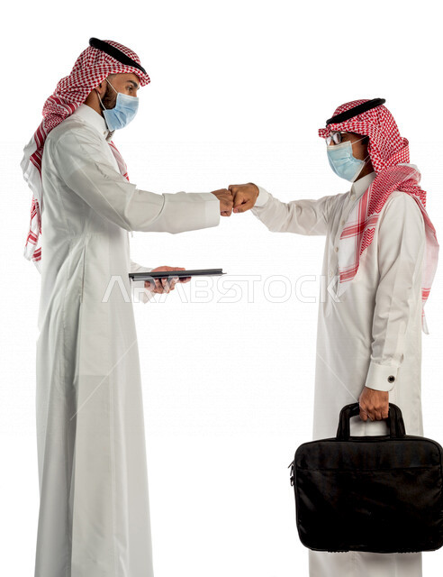 بورتريه لموظفان خليجيان سعوديان يتصافحان بإيماءات يدين مختلفة، إرتداء القناع الطبي الوقائي للوقاية من فايروس كورونا كوفيد-19، إستخدام جهاز التابلت، زملاء عمل، مفهوم إدارة الأعمال، صفقات عمل، إتباع إجراءات الوقاية والحماية من الفيروسات، الحفاظ على المسافات
