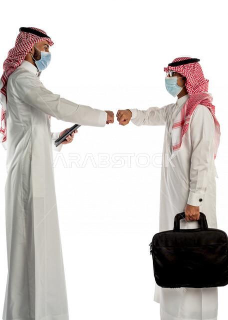 بورتريه لموظفان خليجيان سعوديان يتصافحان بإيماءات يدين مختلفة، إرتداء القناع الطبي الوقائي للوقاية من فايروس كورونا كوفيد-19، إستخدام جهاز التابلت، زملاء عمل، مفهوم إدارة الأعمال، صفقات عمل، إتباع إجراءات الوقاية والحماية من الفيروسات، الحفاظ على المسافات