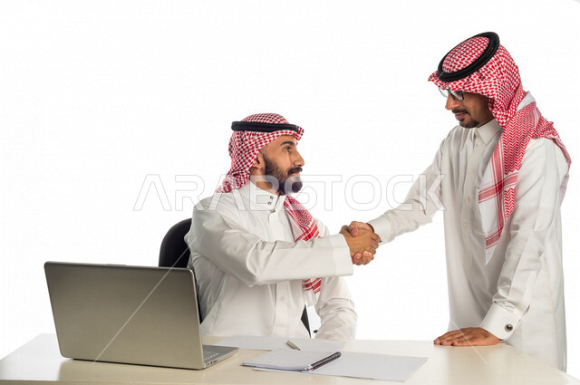 بورتريه لموظفان خليجيان سعوديان في مقر العمل يتصافحان، إستخدام الحاسوب المحمول لإنجاز المهام، زملاء عمل، مفهوم إدارة الأعمال، جلسة عمل ، الإتفاق والشراكة على الأعمال والمشاريع التجارية، أعمال مكتبية، صفقات تجارية، بيئه عمل، متابعة ومناقشة العمل