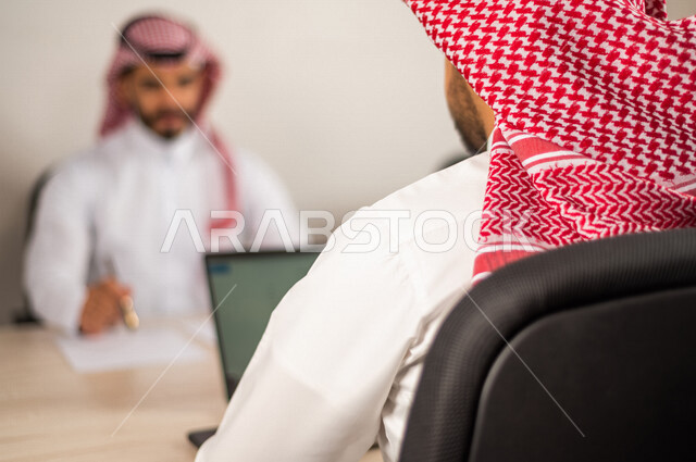 موظفان عربيان سعوديان خليجيان يعملان في  مقر الشركه, مناقشة وانجاز الاعمال عبر جهاز اللابتوب, تحقيق اهداف الشركه, تطوير العمل, بيئة العمل السعودي