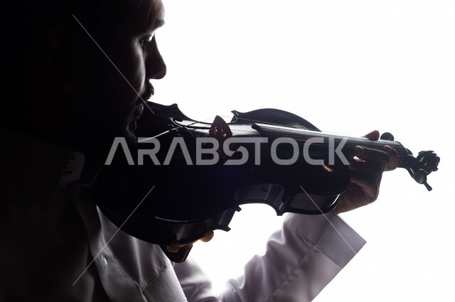 صورة ظلية لرجل عربي سعودي خليجي يقوم بالعزف على آلة الكمان , آلات موسيقية , بورتريه لشاب يمارس هواية العزف , مواهب موسيقية .