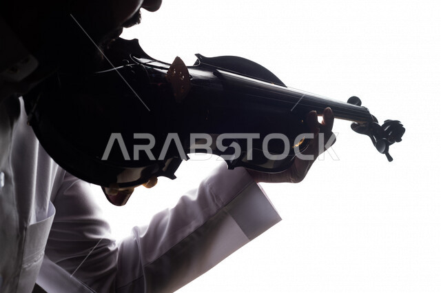 صورة ظلية لرجل عربي سعودي خليجي يقوم بالعزف على آلة الكمان , آلات موسيقية , بورتريه لشاب يمارس هواية العزف , مواهب موسيقية .