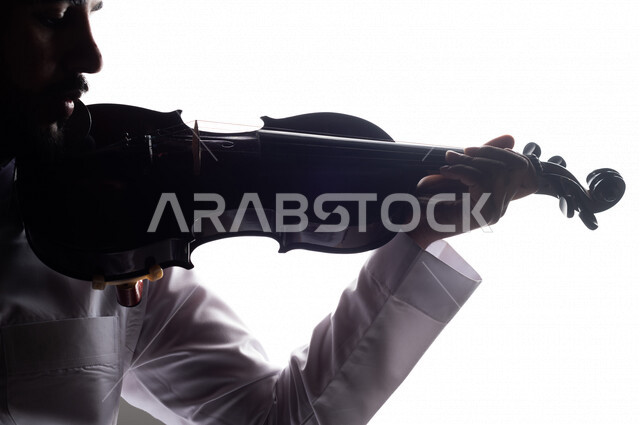 صورة ظلية لرجل عربي سعودي خليجي يقوم بالعزف على آلة الكمان , آلات موسيقية , بورتريه لشاب يمارس هواية العزف , مواهب موسيقية .