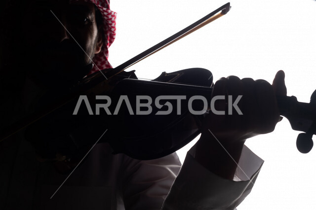 صورة ظلية لرجل عربي سعودي خليجي يقوم بالعزف على آلة الكمان , آلات موسيقية , بورتريه لشاب يمارس هواية العزف , مواهب موسيقية .