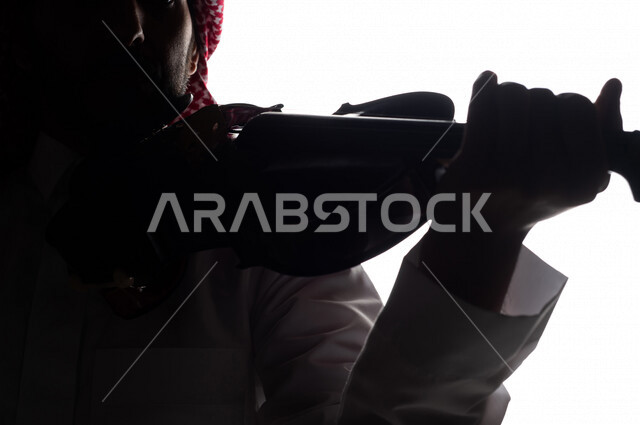 صورة ظلية لرجل عربي سعودي خليجي يقوم بالعزف على آلة الكمان , آلات موسيقية , بورتريه لشاب يمارس هواية العزف , مواهب موسيقية .