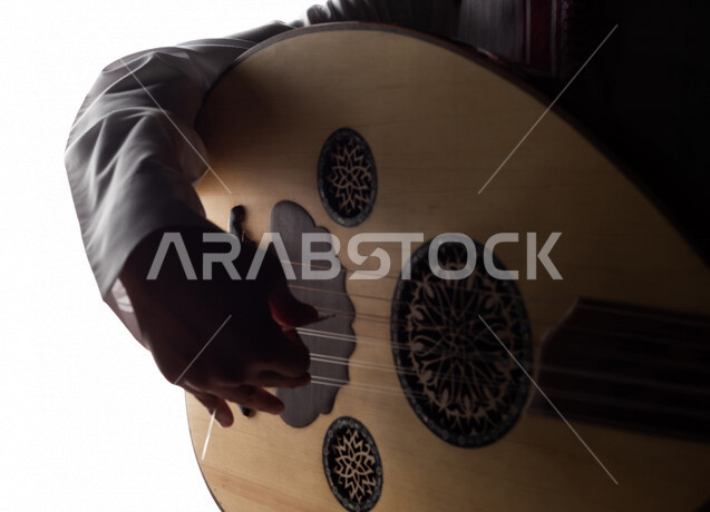 صورة ظلية لرجل عربي سعودي خليجي يقوم بالعزف على آلة العود , آلات موسيقية , بورتريه لشاب يمارس هواية العزف , مواهب فنية , فنون موسيقية .