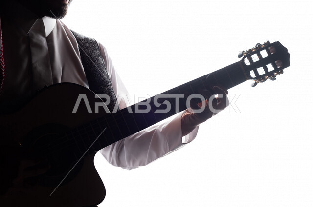صورة ظلية لرجل عربي سعودي خليجي يقوم بالعزف على آلة القيثارة , آلات موسيقية , بورتريه لشاب يمارس هواية العزف , فنون موسيقية , مواهب فنية.