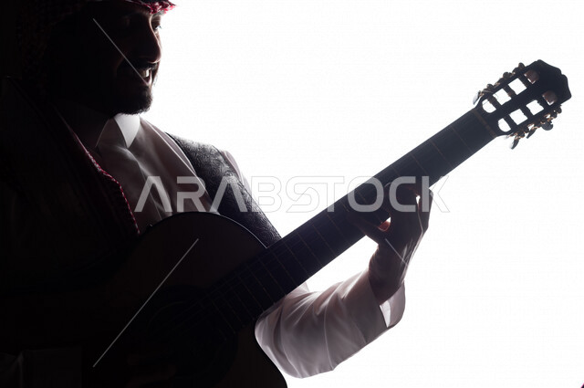 صورة ظلية لرجل عربي سعودي خليجي يقوم بالعزف على آلة القيثارة , آلات موسيقية , بورتريه لشاب يمارس هواية العزف , فنون موسيقية , مواهب فنية.