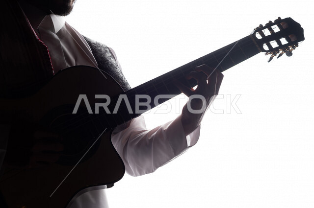 صورة ظلية لرجل عربي سعودي خليجي يقوم بالعزف على آلة القيثارة , آلات موسيقية , بورتريه لشاب يمارس هواية العزف , فنون موسيقية , مواهب فنية.