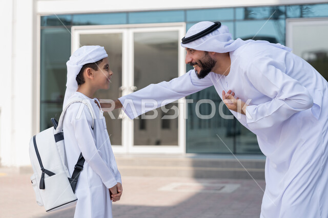 إلقاء عبارات التشجيع الداعمة في أول أيام الدوام المدرسي، إعطاء الدعم النفسي والتحفيز المعنوي للأبناء، موسم العودة إلى المدارس بالامارات العربية المتحدة، مفهوم الأبوة والحنان، ولد عربي خليجي إماراتي يرتدي الكندورة والعمامة وحقيبة الظهر المدرسية برفقة والده