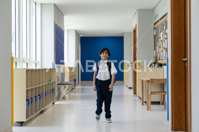 موسم العودة إلى المدارس، السعي نحو تحقيق التفوق والنجاح، التوجه إلى الصف بسعادة وتفاؤل، تلميذ عربي خليجي إماراتي يرتدي الزي المدرسي ويحمل حقيبة الظهر يقف في ممر المدرسة، التعليم الأكاديمي في المؤسسات التعليمية في الامارات، البدء بعام دراسي جديد بإيماءات الحماس