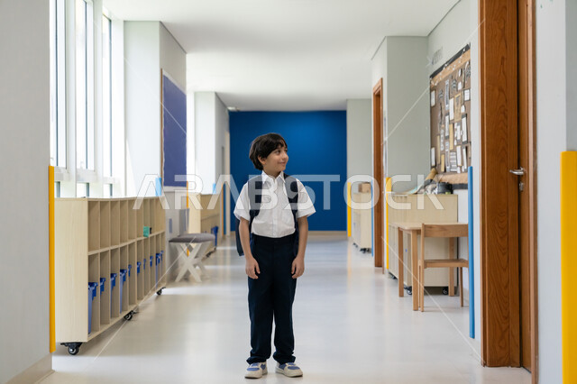 البدء بعام دراسي جديد بإيماءات الحماس، موسم العودة إلى المدارس، السعي نحو تحقيق التفوق والنجاح، التوجه إلى الصف بسعادة وتفاؤل، تلميذ عربي خليجي إماراتي يرتدي الزي المدرسي ويحمل حقيبة الظهر يقف في ممر المدرسة، التعليم الأكاديمي في المؤسسات التعليمية في الامارات