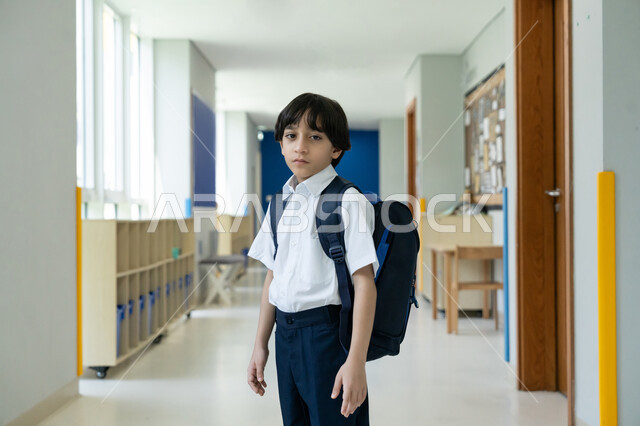 التعليم الأكاديمي في المؤسسات التعليمية في الامارات، البدء بعام دراسي جديد بإيماءات الحماس، السعي نحو تحقيق التفوق والنجاح، التوجه إلى الصف بسعادة وتفاؤل، صورة مقربة لتلميذ عربي خليجي إماراتي يرتدي الزي المدرسي ويحمل حقيبة الظهر يقف في ممر المدرسة