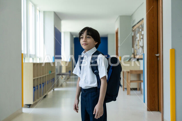 المؤسسات التعليمية المتطورة في الامارات العربية المتحدة، البدء بعام دراسي جديد بإيماءات الحماس، السعي نحو تحقيق التفوق والنجاح، التوجه إلى الصف بسعادة وتفاؤل، صورة مقربة لتلميذ عربي خليجي إماراتي يرتدي الزي المدرسي ويحمل حقيبة الظهر يقف في ممر المدرسة