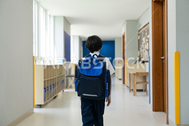 المشي نحو الصف بسعادة وتفاؤل، المؤسسات التعليمية المتطورة في الامارات العربية المتحدة، البدء بعام دراسي جديد بإيماءات الحماس، السعي نحو تحقيق التفوق والنجاح، صورة مقربة من الخلف لتلميذ عربي خليجي إماراتي يرتدي الزي المدرسي ويحمل حقيبة الظهر يقف في ممر المدرسة