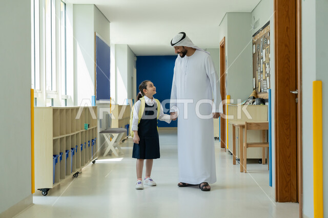 رعاية الأولاد وتقديم الدعم والتشجيع لهم في بداية السنة الدراسية، الحضور المبكر للحصص المدرسية، السعادة والحماس بالعودة إلى المدرسة، أب عربي خليجي إماراتي يرتدي الكندورة والغترة يرافق ابنته إلى المدرسة في يومها الدراسي الأول، تلميذة مرتبة تحمل حقيبة الظهر بفرح