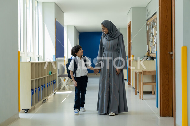 الاهتمام بتعليم ودعم الأبناء نفسيا، تعابير السعادة والحماس لبدأ العام الدراسي الجديد، الحضور المبكر للحصص المدرسية، أم عربية خليجية إماراتية محجبة ترتدي عباءة رمادية ترافق ابنها في يومه الدراسي الأول، تلميذ إماراتي يرتدي الزي المدرسي ويحمل حقيبة الظهر بفرح