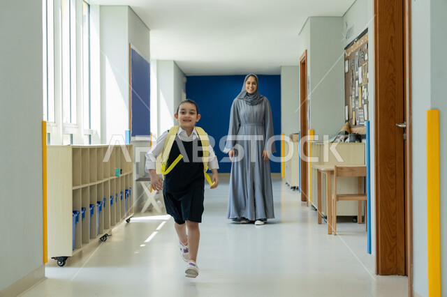 الحضور المبكر للحصص المدرسية، إيصال الأبناء إلى المدرسة، أم عربية خليجية إماراتية محجبة ترتدي عباءة رمادية ترافق ابنتها في يومها الدراسي الأول، التربية الحديثة وتقديم الدعم والتشجيع في بداية السنة الدراسية، تلميذة ترتدي الزي المدرسي وتحمل حقيبة الظهر بفرح