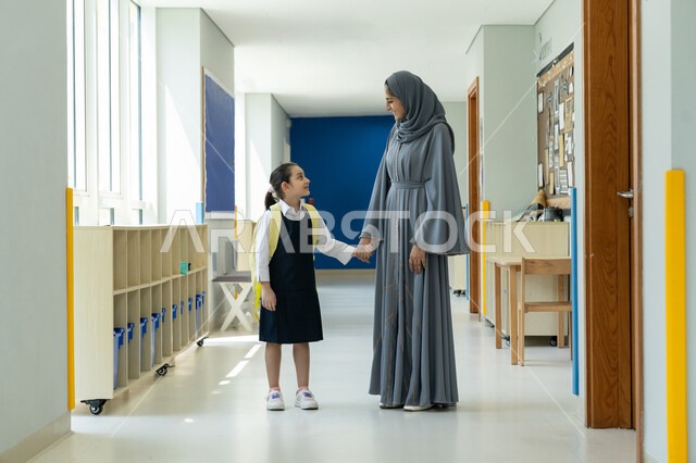 التربية الحديثة وتقديم الدعم والتشجيع في بداية السنة الدراسية، الحضور المبكر للحصص المدرسية، إيصال الأبناء إلى المدرسة، أم عربية خليجية إماراتية محجبة ترتدي عباءة رمادية ترافق ابنتها في يومها الدراسي الأول، تلميذة ترتدي الزي المدرسي وتحمل حقيبة الظهر بفرح