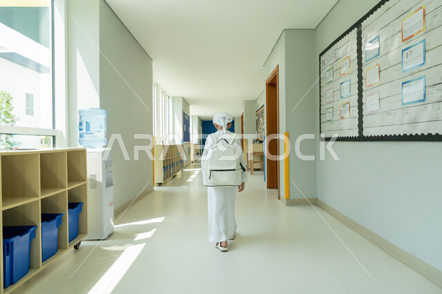 السعي نحو تحقيق التفوق والنجاح، التوجه إلى الصف بسعادة وتفاؤل، صوة من الخلف لتلميذ عربي خليجي إماراتي يرتدي الكندورة والعمامة ويحمل حقيبة الظهر يمشي في الممر المدرسي، التعليم الأكاديمي في المؤسسات التعليمية في الامارات العربية المتحدة، موسم العودة إلى المدارس