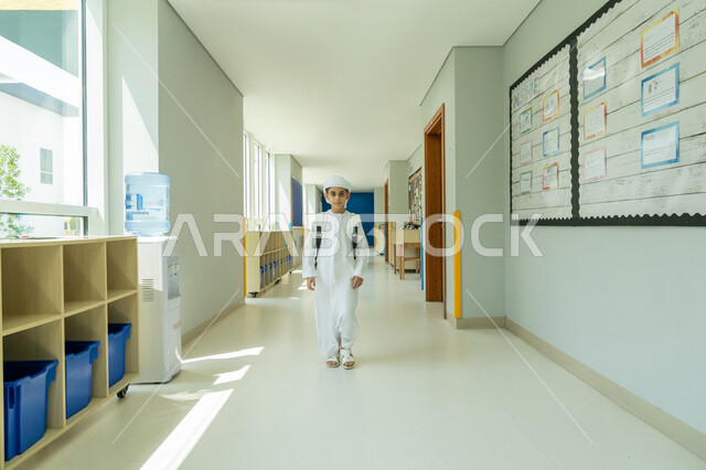 التوجه إلى الصف بسعادة وتفاؤل، تلميذ عربي خليجي إماراتي يرتدي الكندورة والعمامة ويحمل حقيبة الظهر يمشي في الممر المدرسي، السعي نحو تحقيق التفوق والنجاح، التعليم الأكاديمي في المؤسسات التعليمية في الامارات العربية المتحدة، انطلاق موسم العودة إلى المدارس