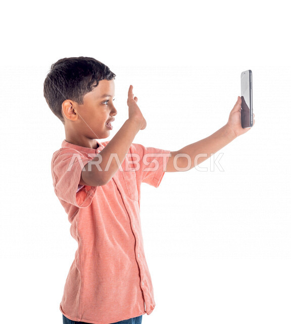 بورتريه لفتى عربي خليجي سعودي يستخدم الهاتف المحمول ،التقاط صورة سيلفي ، اجراء مكالمة فيديو ، خلفية بيضاء