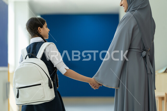 الاهتمام بتعليم وتطوير الأولاد ودعمهم، صورة من الخلف لام عربية خليجية إماراتية تمسك يد ابنتها  وتمشي في الممر، إسداء النصائح والتشجيع في أول أيام الدوام المدرسي، إعطاء الدعم النفسي والتحفيز المعنوي للأبناء، رابط الأمومة والحنان، الحضور المبكر للحصص المدرسية