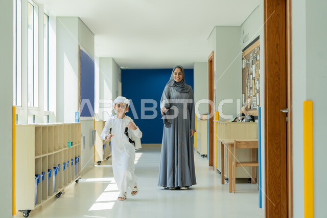 تقديم الرعاية والاهتمام بالأبناء، انطلاق العام الدراسي الجديد بمدارس الامارات العربية المتحدة، توصيل الأم لابنها من وإلى المدرسة، ولد عربي خليجي إمارتي يرتدي الكندورة والغترة وحقيبة الظهر يركض برفقة أمه في ممر المدرسة، مفهوم الأمومة والحب والحنان