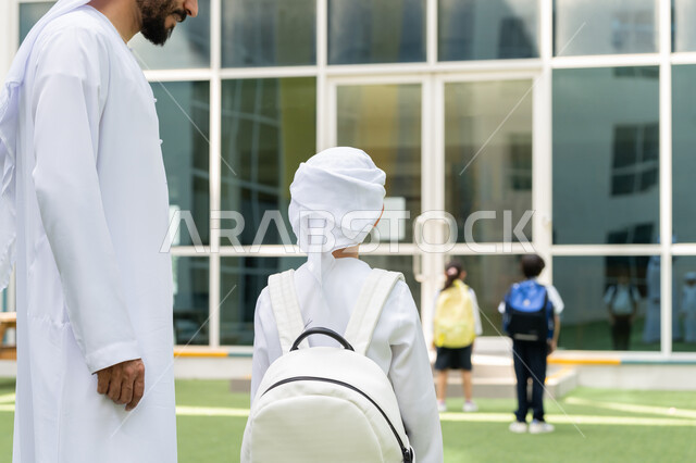 إلقاء عبارات التشجيع الداعمة في أول أيام الدوام المدرسي، إعطاء الدعم النفسي والتحفيز المعنوي للأبناء، موسم العودة إلى المدارس بالامارات العربية المتحدة، مفهوم الأبوة والحنان، ولد عربي خليجي إماراتي يرتدي الكندورة والغترة ويلبس حقيبة الظهر المدرسية برفقة والده