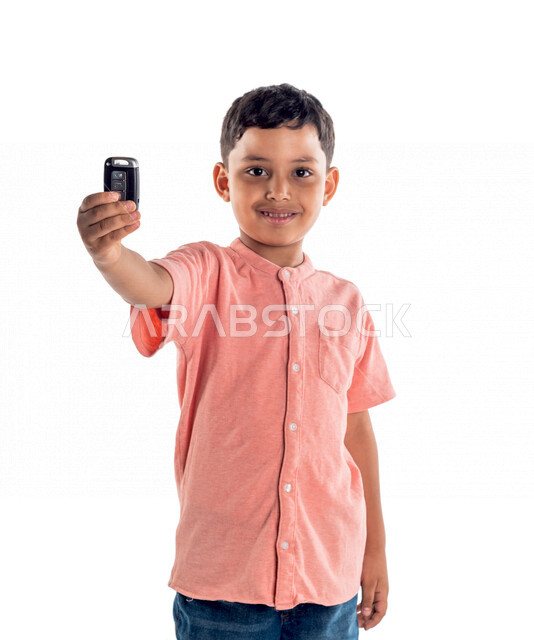 Portrait of a Saudi Gulf boy holding a car remote control in his hand, facial expressions indicating happiness and joy, white background
