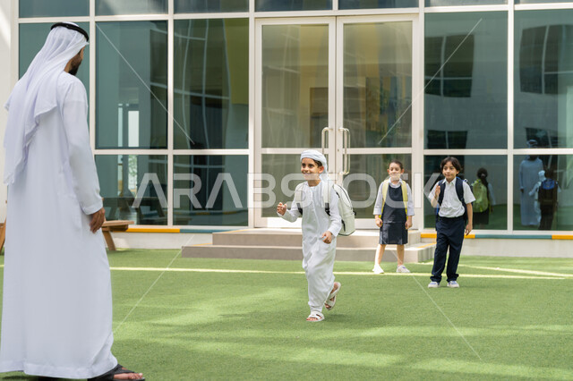 توصيل الأب للأبناء من وإلى المدرسة، انطلاق العام الدراسي الجديد في مدارس الامارات العربية المتحدة، ولدعربي خليجي إمارتي يرتدي الكندورة والغترة يقف برفقة والده أمام المدرسة، إلقاء عبارات التشجيع الداعمة والمحفزة للأولاد في أول أيام الدوام المدرسي