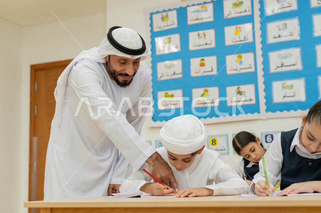 The concept of diligence and striving for excellence, the importance of knowledge in developing mental abilities, gestures of concentration, contemplation and focus, education in the United Arab Emirates, an Arab Gulf Emirati teacher wearing a kandura and a ghutra helping students during exams
