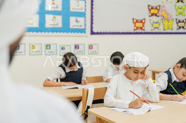 Achievement and success in the educational stage, an Arab Gulf Emirati teacher wearing a kandura and a ghutra monitoring students during an exam, education in the United Arab Emirates, diligent students solving questions with gestures of concentration and contemplation, end-of-semester exams