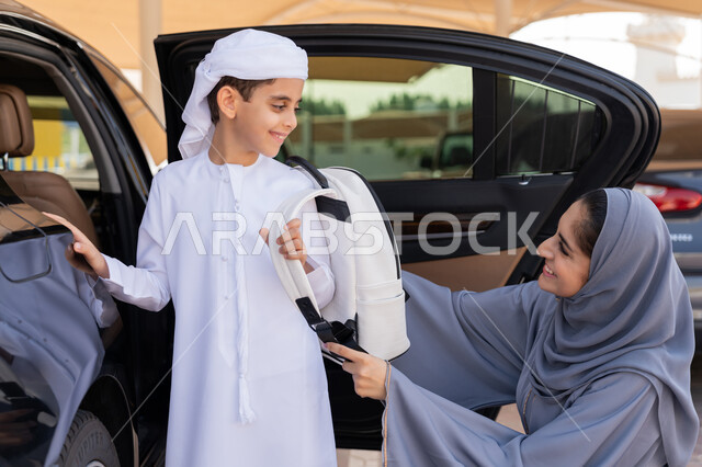 الاهتمام بتعليم وتطوير الابناء ودعمهم، ام عربية خليجية إماراتية تقوم بتوديع ابنها قبل ركوب السيارة، تلميذ متفوق يرتدي الكندورة والعمامة البيضاء يستعد للذهاب الى المدرسة بإيماءات الحماس والسرور، التعليم الحديث في الامارات، الحضور المبكر للحصص المدرسية