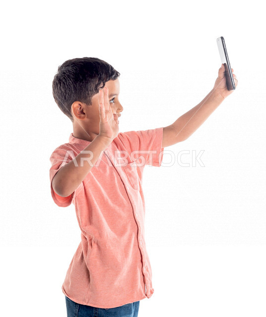 بورتريه لفتى عربي خليجي سعودي يستخدم الهاتف المحمول ،التقاط صورة سيلفي ، اجراء مكالمة فيديو ، خلفية بيضاء