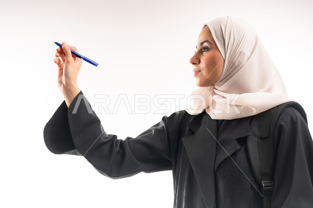 Concept of drawing and sketching, getting ready to write down and outline something, close-up portrait of a veiled Saudi Arabian Gulf university student carrying a backpack holding a pen and making writing gestures in the air, white background