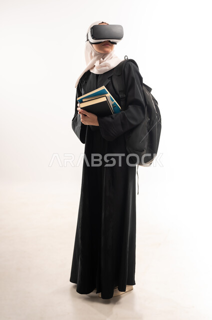 Virtual world simulation, integration of modern technologies with learning and training, education using virtual world technology, side portrait of a veiled Saudi Arabian Gulf university student wearing a backpack, 3D VR glasses, holding a set of books, full body image, white background