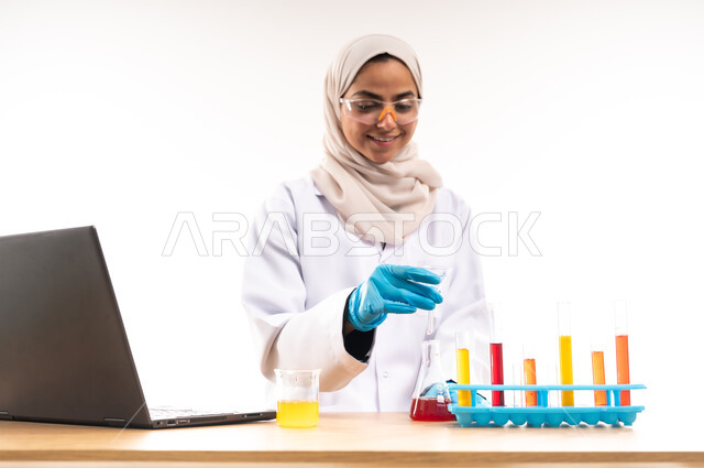 Integrating modern devices and technology into practical life, close-up portrait of smiling Saudi Arabian Gulf female university student wearing white coat and glasses using test tubes to conduct scientific experiments in the laboratory, concept of biochemistry and research and development, white background