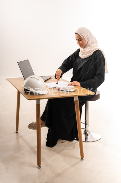 دمج التكنولوجيا في المجال التعليمي, الدراسة والاجتهاد والتفوق, المناهج والمواد التعليمية، التعليم الجامعي في السعودية، بورتريه لطالبة جامعية عربية خليجية سعودية محجبة ترتدي العباءة تدرس في قسم الهندسة والانشاء, تدقيق وتصميم المشروع الهندسي, خلفية بيضاء
