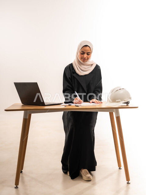 التعليم الجامعي في السعودية، بورتريه لطالبة جامعية عربية خليجية سعودية محجبة ترتدي العباءة تدرس في قسم الهندسة والانشاء, تدقيق وتصميم المشروع الهندسي, دمج التكنولوجيا في المجال التعليمي, الدراسة والاجتهاد والتفوق, المناهج والمواد التعليمية، خلفية بيضاء