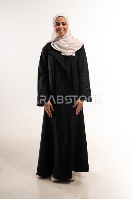 الاهتمام بالأناقة والمظهر الخارجي، بورتريه لشابة عربية خليجية سعودية محجبة مبتسمة ترتدي العباءة تنظر الى الكاميرا، ايماءات السعادة والسرور، التقاط صور شخصية للوثائق الرسمية، الوقوف باستقامة واعتدال، مفهوم الأنوثة والثقة بالنفس، الطول الكامل للجسم، خلفيةبيضاء