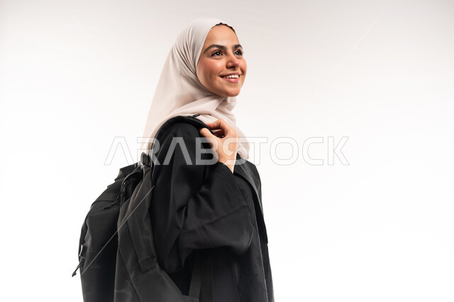 الاستعداد للعام الجامعي الجديد, تعابيرر البشاشة والحماس، التعليم العالي في الجامعات والكليات الأكاديمية في السعودية, بورتريه مقرب لطالبة جامعية عربية خليجية سعودية محجبة ترتدي العباءة وتضع حقيبة الظهر، النظر الى شيء ما بإيماءات السعادة والسرور, خلفية بيضاء