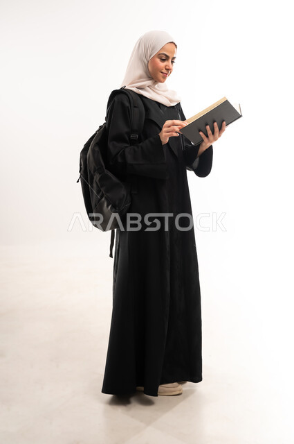 University education in the Kingdom, reviewing daily lessons, the concept of diligence and excellence, a portrait of a veiled Saudi Arabian Gulf university student wearing an abaya carrying a bag on her back, studying lectures and preparing scientific research, interest in browsing useful books, full body length, white background