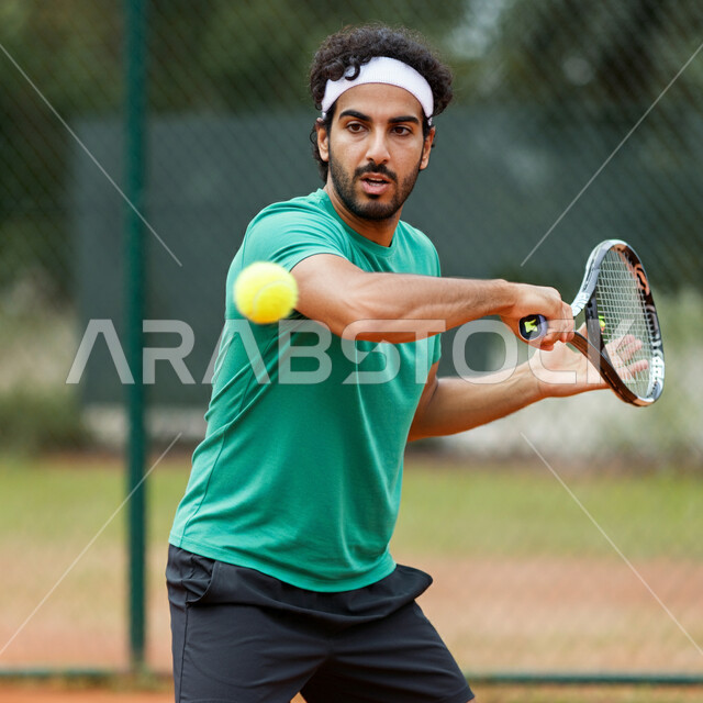 ممارسة لعبة كرة التنس، تدريبات وتمرينات رياضة المضرب، رياضات شبابية وأنشطة ترفيهية، ايماءات تدل على الحماس والاندماج، شاب عربي خليجي سعودي يرتدي الملابس الرياضية يحمل بيده المضرب في الملعب باحتراف وإتقان