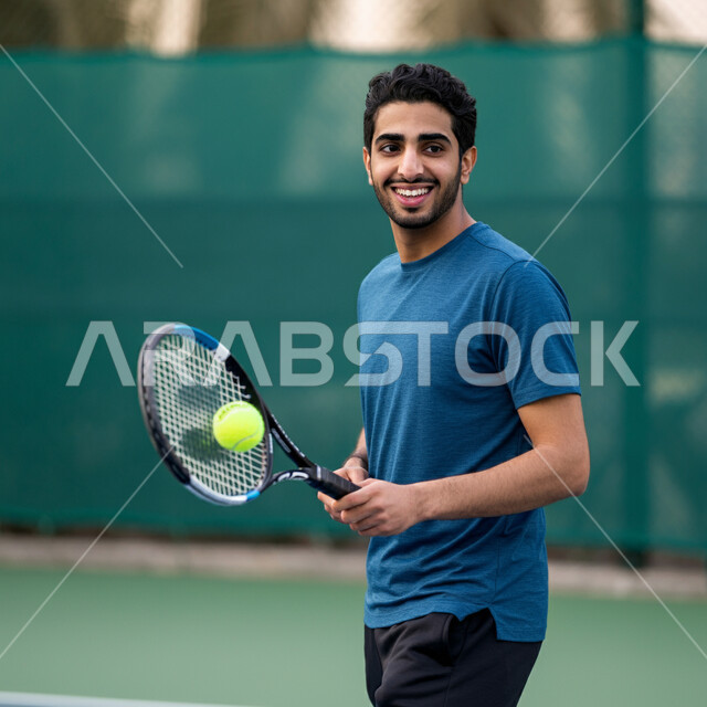 تعابير وايماءات تدل على الحماس والاندماج، شاب عربي خليجي سعودي يرتدي الملابس الرياضية يحمل بيده المضرب في الملعب باحتراف وإتقان، ممارسة لعبة كرة التنس، تدريبات وتمرينات رياضة المضرب، رياضات شبابية وأنشطة ترفيهية